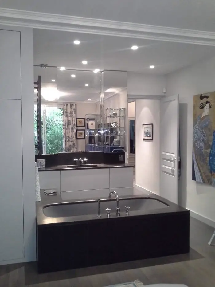 Salle de bain avec baignoire habillée de panneaux sombres, ouverte sur la cuisine