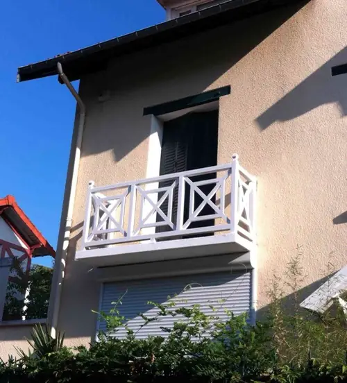 Garde-corps en bois peint blanc à motifs croisés, sur le balcon d’un pavillon