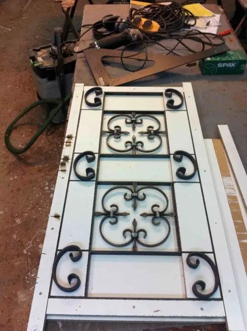 Grille en fer forgé posée à plat sur une porte vitrée, à l’atelier